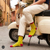 Chillies crew socks styled with cream trousers seated on a vintage scooter on a cobbled street – Dynamocks