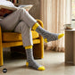 Rogue folk-pattern crew socks worn with light grey chinos on a mustard yellow ottoman — Dynamocks