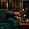 Orange and olive striped crew socks for men styled with black formal trousers and brown loafers on a green velvet sofa — Dynamocks India