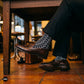 Trios geometric crew socks paired with charcoal trousers and brown penny loafers in a warm cafe interior — Dynamocks